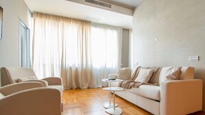 Una sala de estar moderna con un sofá, sillas, una mesa de centro y un ventanal con cortinas.