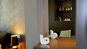 Un baño moderno con un espejo grande, una silla blanca, una mesita con una lámpara y un adorno en la pared.