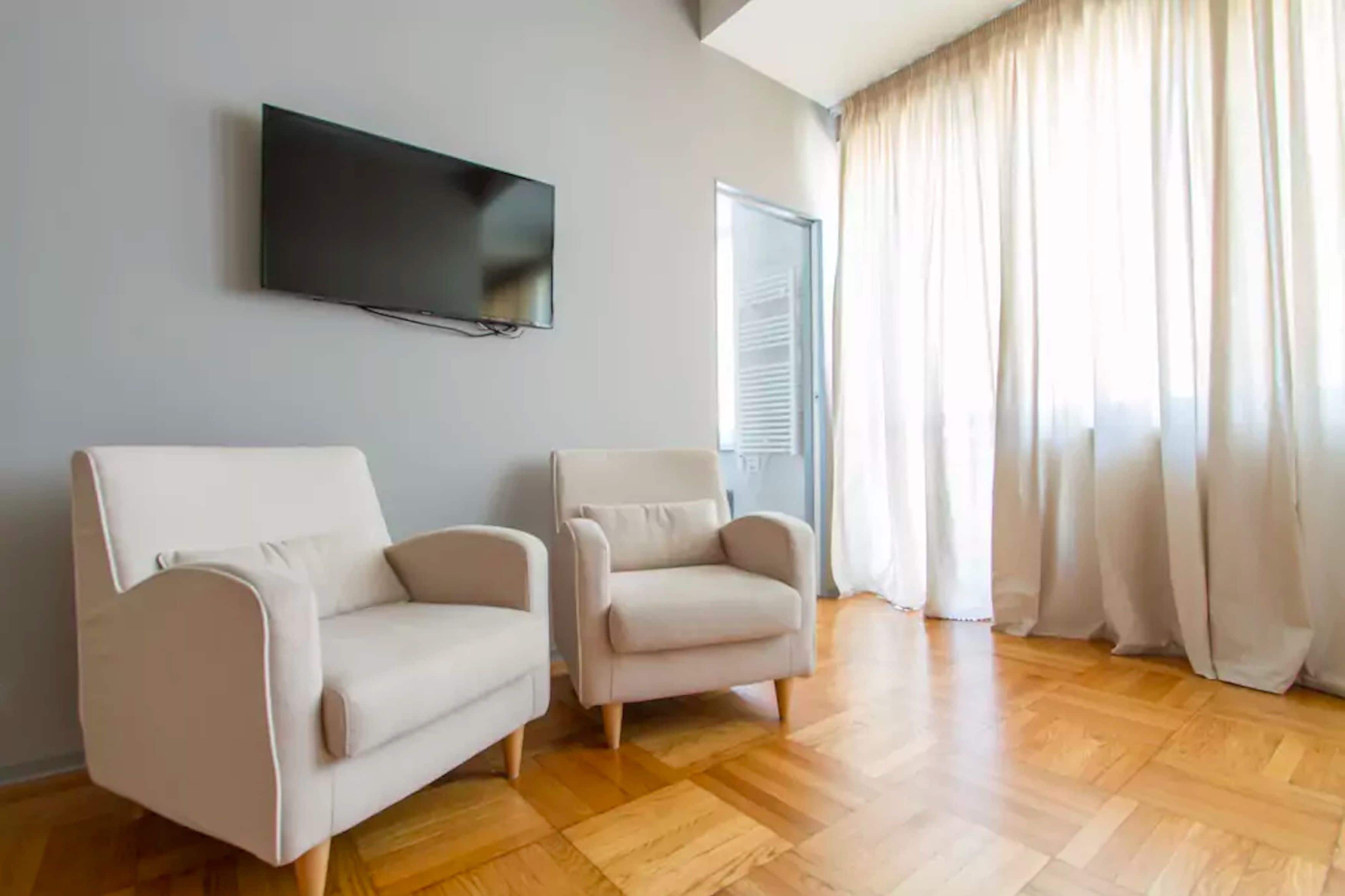 Un salon avec deux canapés, un téléviseur à écran plat fixé au mur et une fenêtre avec des rideaux.