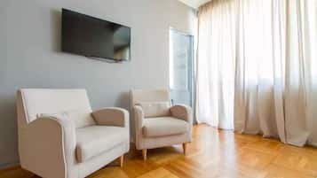 Ein Wohnzimmer mit zwei Sofas, einem Wandfernseher und einem Fenster mit Vorhängen.