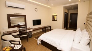 A modern hotel room with a large bed, a desk with a chair, a flat-screen TV, an air conditioner, and a ceiling fan. - Hotel One Rahim Yar Khan Club Road (Rahim Yar Khan)
