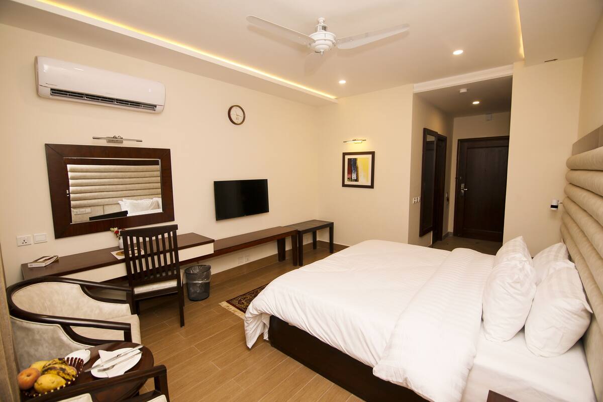 Une chambre d’hôtel moderne dotée d’un grand lit, d’un bureau avec une chaise, d’un téléviseur à écran plat, d’un climatiseur et d’un ventilateur de plafond.