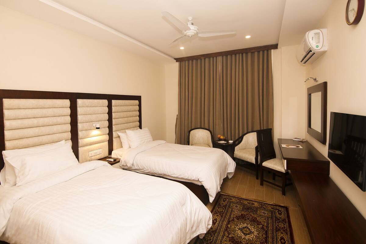 Une chambre d’hôtel avec deux lits, un bureau, une chaise, une télévision et un ventilateur de plafond.