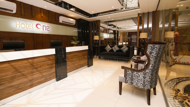 A hotel reception area with a wooden reception desk, a black and white patterned armchair, and a black sofa with zebra print cushions. - Hotel One Rahim Yar Khan Club Road (Rahim Yar Khan)