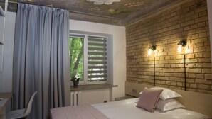 A bedroom with a brick wall, a window with blinds, a bed with pillows, a chair, and a radiator. - Stan Gret Hotel (Kyiv)