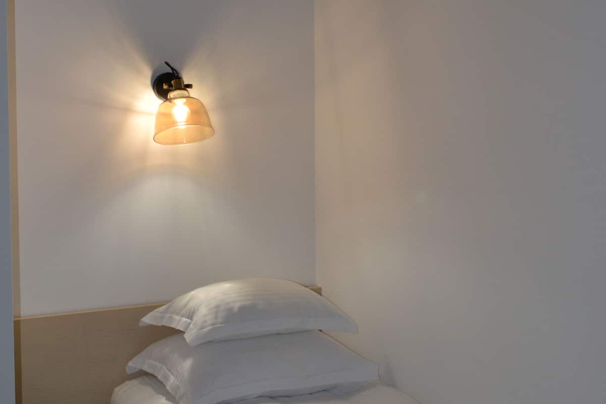 Una cama individual con ropa de cama y almohadas blancas, una mesita de noche con lámpara y un techo con diseño floral.