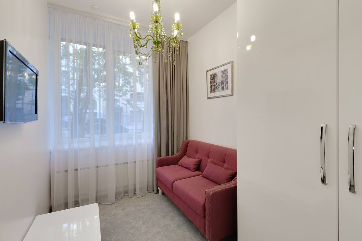 Una sala de estar moderna con un sofá rojo, un televisor blanco, una araña y cortinas traslúcidas.