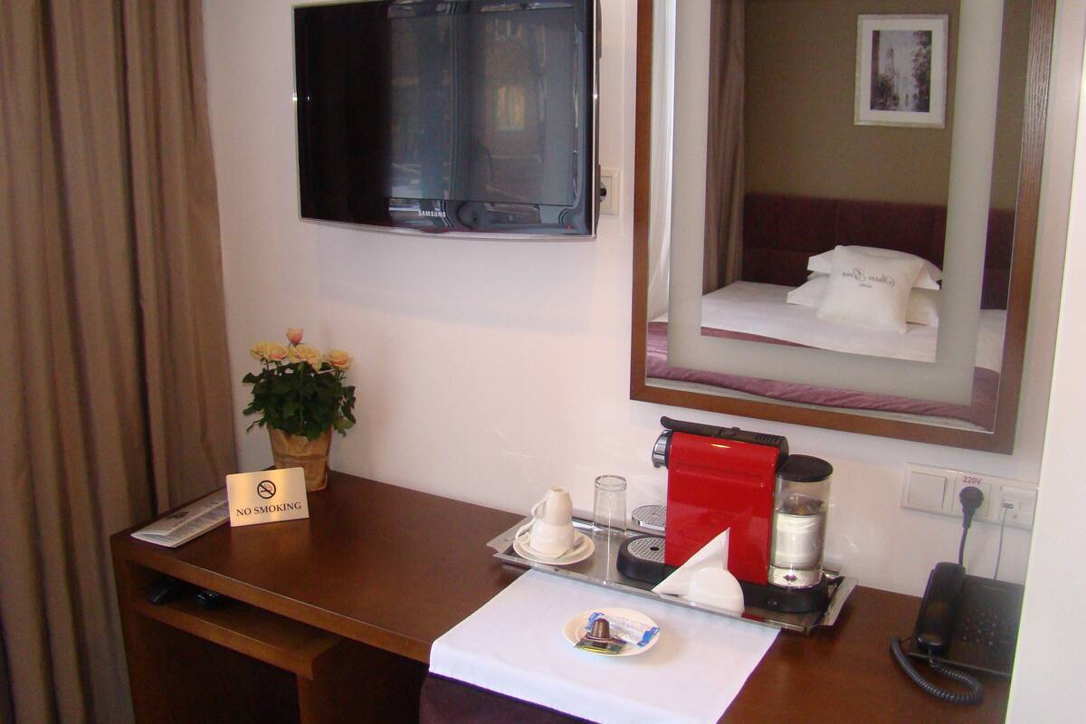 Habitación de hotel con televisor, cama, mesita de noche con cafetera, teléfono y un cartel de 'No Fumar'.