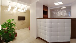 A reception area with a white tufted headboard, a potted plant, and a projection screen displaying a horse-drawn carriage. - Stan Gret Hotel (Kyiv)