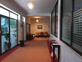 Un hall de hotel con alfombra roja, un sofá, una mesa de centro y un cuadro enmarcado en la pared.