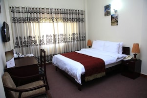 Una habitación de hotel con una cama, un escritorio, una silla, una lámpara y dos cuadros en la pared.