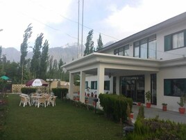 Un hotel con un área de estar exterior cubierta, un letrero que indica un restaurante y vistas a montañas al fondo.