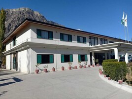 Un edificio de dos pisos con techo plano, ventanas amplias y un acceso pavimentado con plantas en macetas.