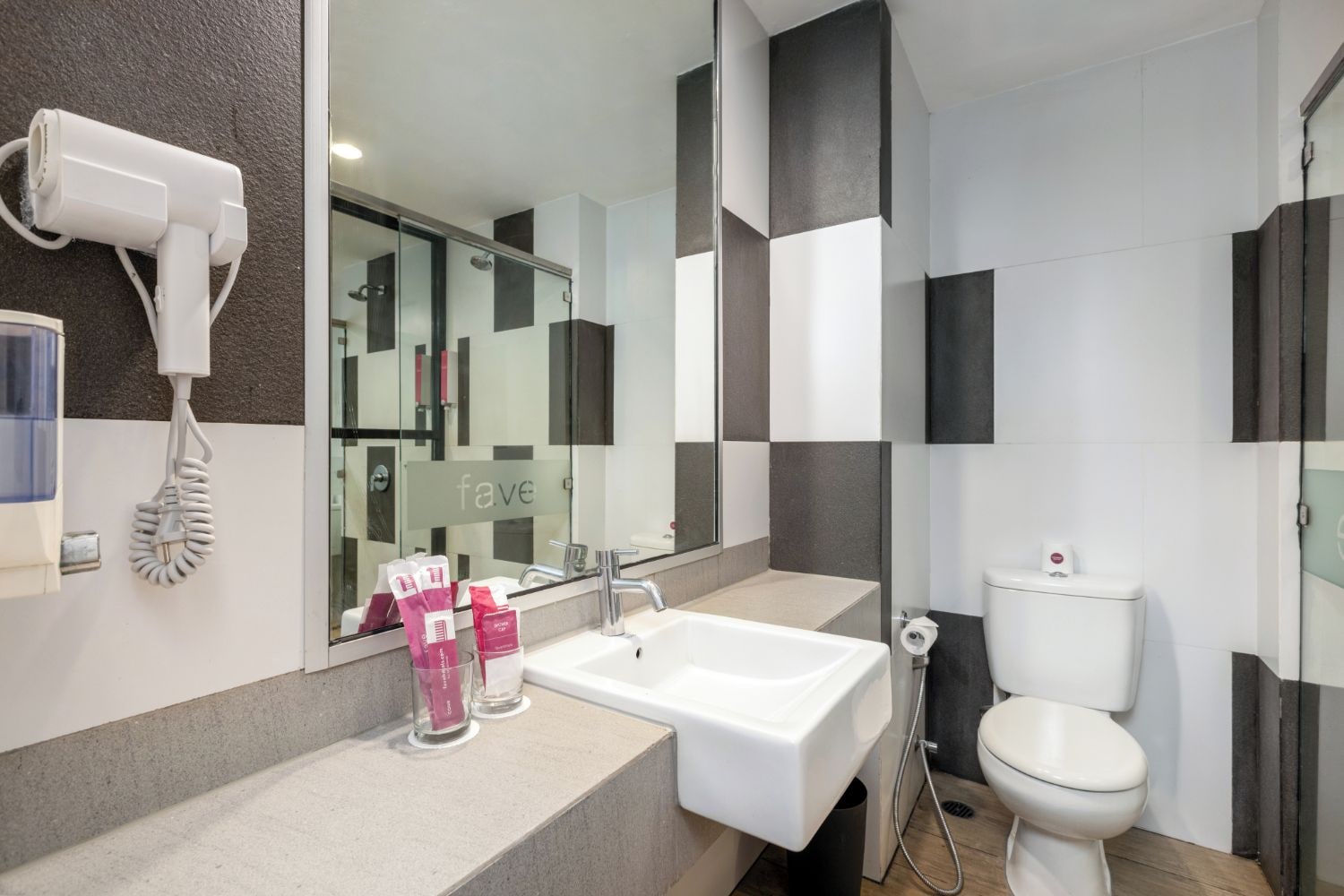Un baño moderno con un lavamanos blanco, un espejo, un secador de pelo y artículos de aseo.