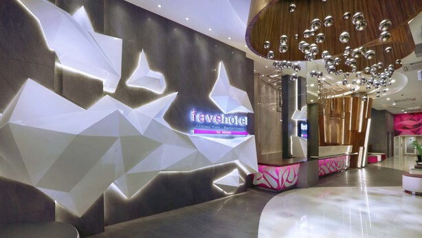 Eine moderne Hotelhalle mit einem geometrischen Wanddesign, einem Empfangstresen und einer Kronleuchter.