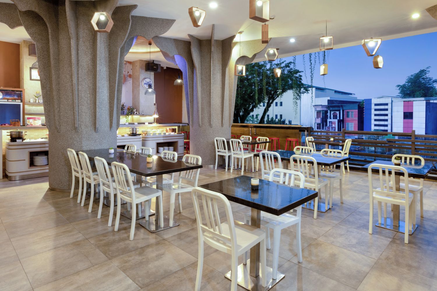 Un restaurant au décor moderne, avec une salle à manger centrale dotée de chaises et de tables blanches, et une cuisine visible à travers une arche.