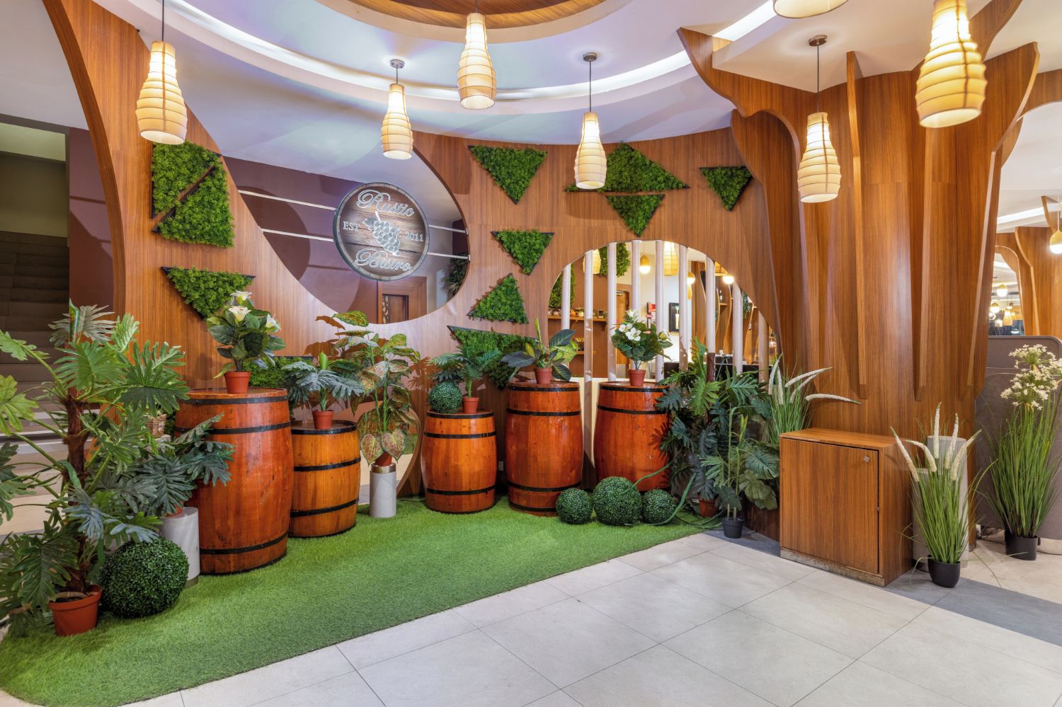 Un espace d’accueil agrémenté de jardinières en forme de tonneaux en bois, de gazon synthétique et d’un comptoir de réception.