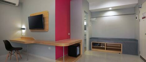 Quarto moderno com escrivaninha curva, TV de tela plana, parede de destaque vermelha e área de estar com um banco e prateleiras.
