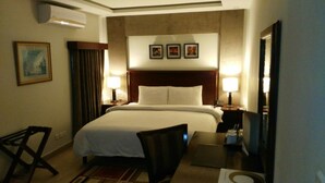 A hotel room with a large bed, two bedside tables with lamps, a chair, a desk, and a mirror. - Hotel One Super Islamabad (Islamabad)
