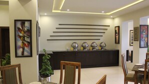 A modern dining area with a long table, chairs, and a dark-colored kitchen in the background. - Hotel One Super Islamabad (Islamabad)