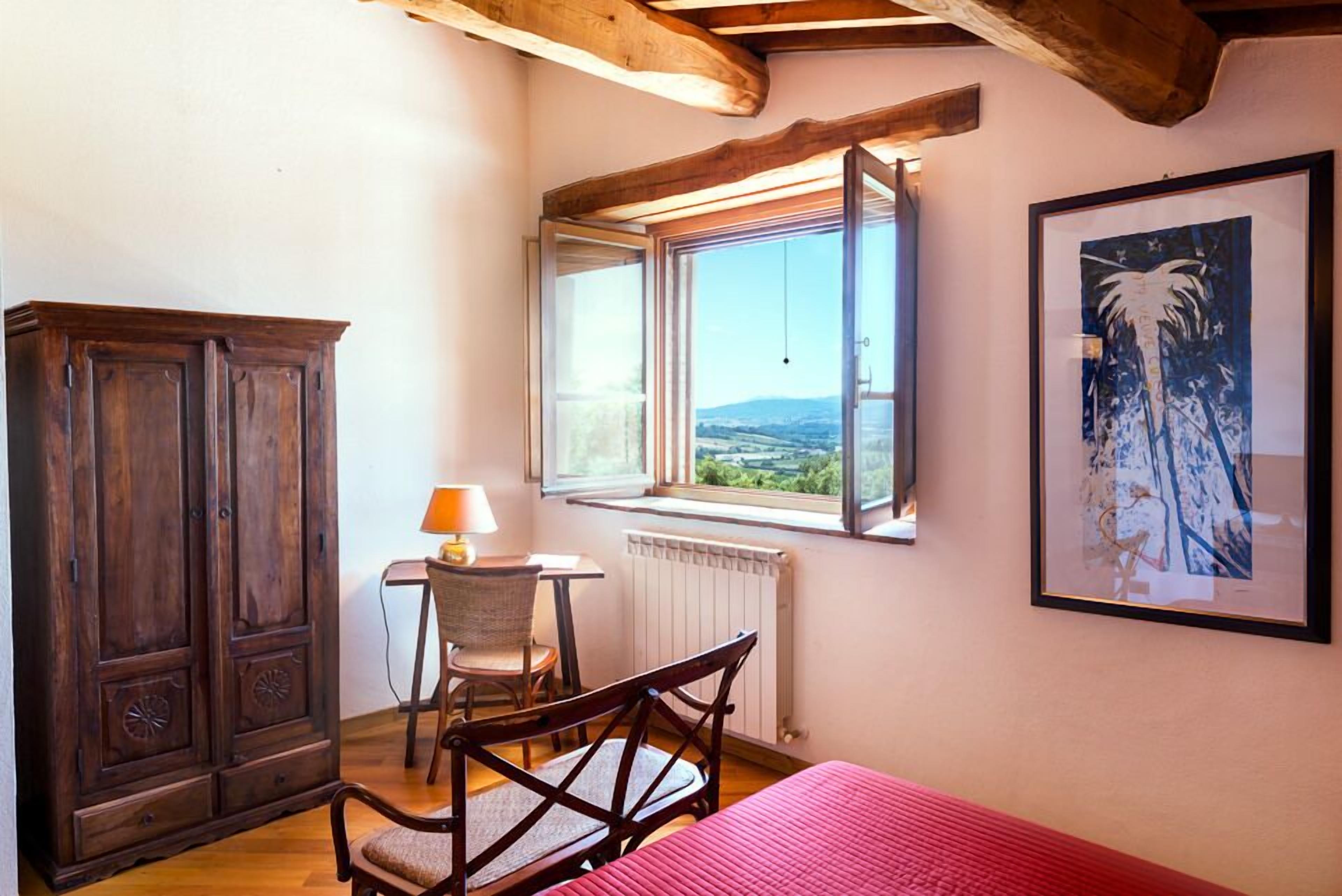 Una habitación con un armario de madera, un escritorio con una silla, una ventana con vistas y un cuadro en la pared.