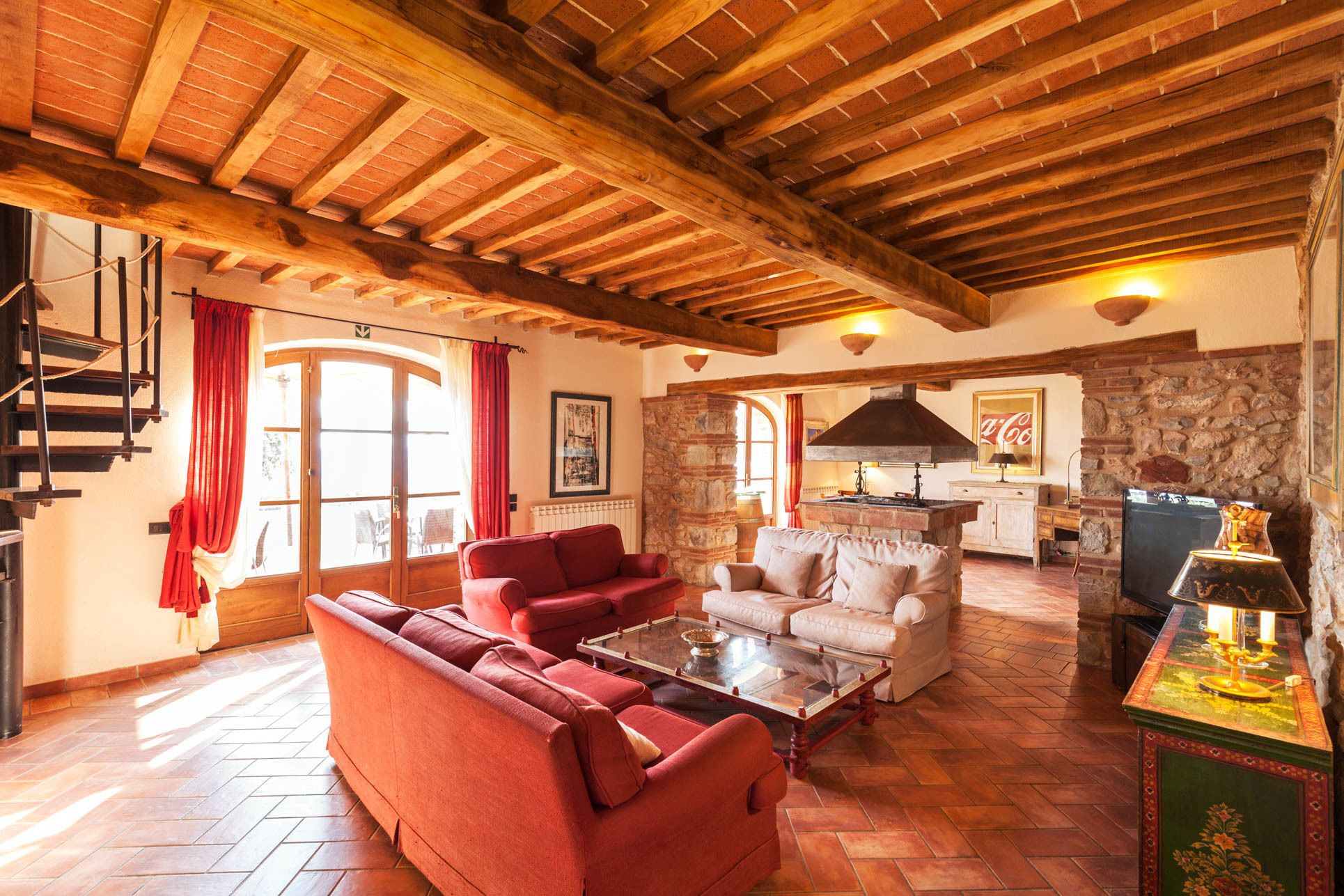 A spacious living area with a wooden ceiling, red sofas, a coffee table, and a stone wall.