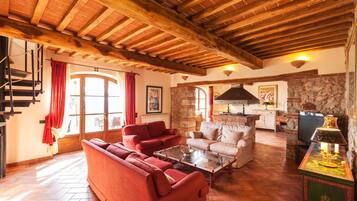 A spacious living area with a wooden ceiling, red sofas, a coffee table, and a stone wall.