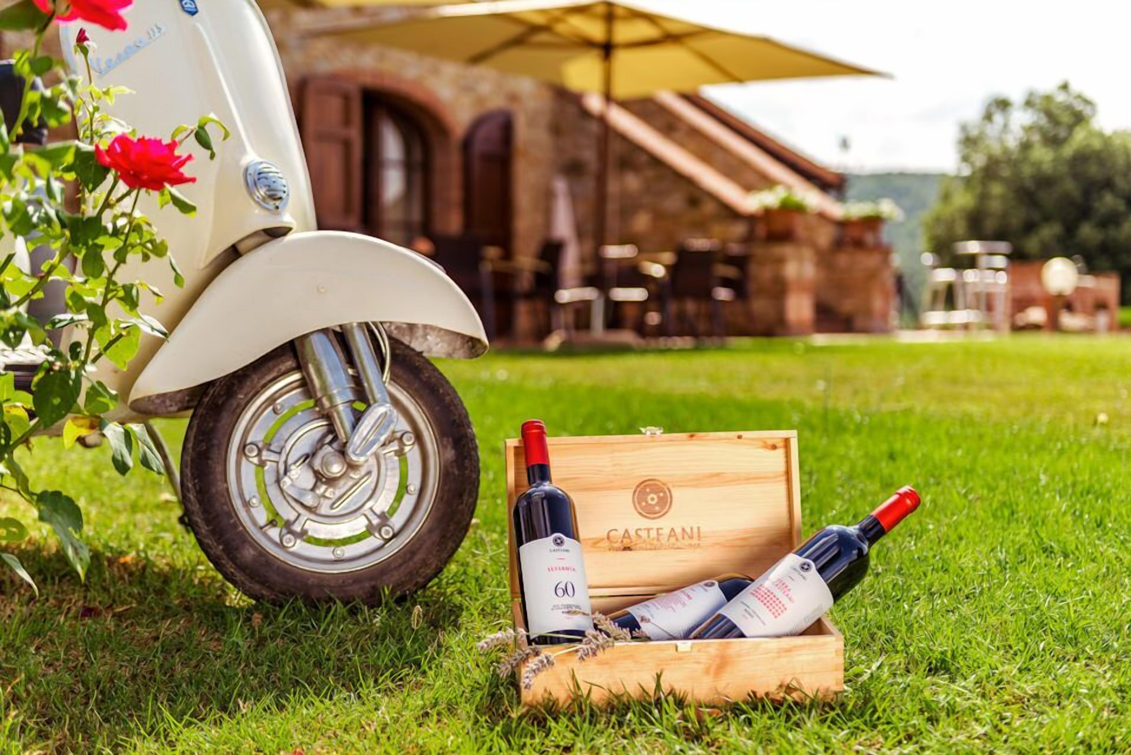 A vintage motorcycle parked on grass with a wooden crate containing bottles of wine labeled "Casteanl."