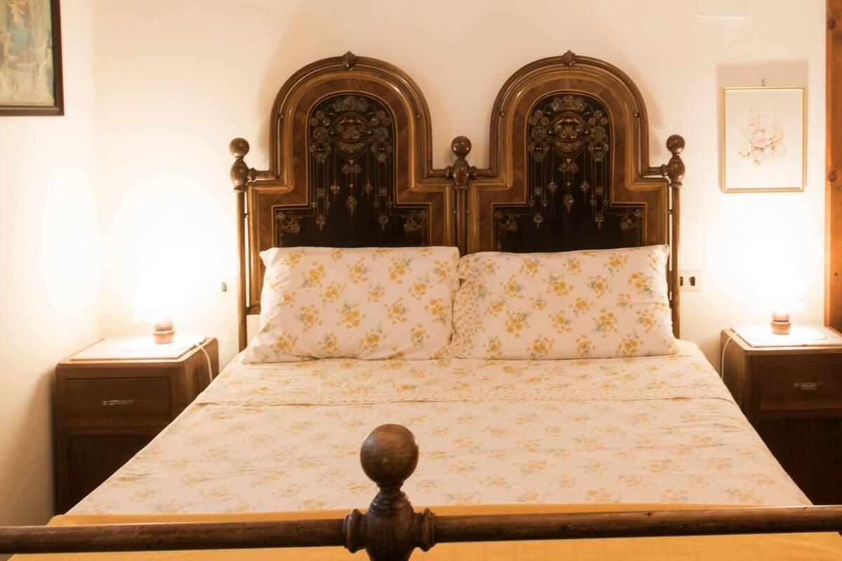 A bed with a floral bedspread and two matching pillows, flanked by wooden nightstands with lamps.