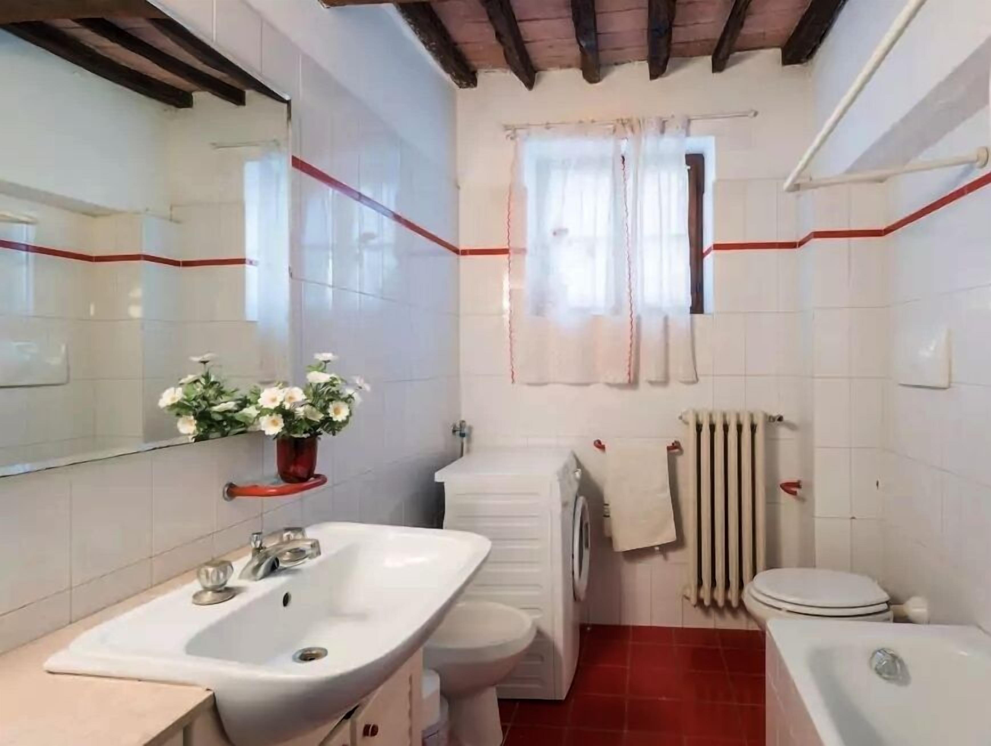 A bathroom with a white sink, toilet, and bathtub, a mirror, and a window with a curtain.