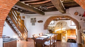 Un interior rústico con una mesa de comedor de madera, una escalera y un muro de piedra.