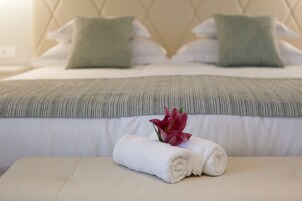 Ein ordentlich bezogenes Bett mit einer grün gestreiften Decke, zwei Kissen und einem aufgerollten weißen Handtuch mit einer roten Blume auf einem Nachttisch.