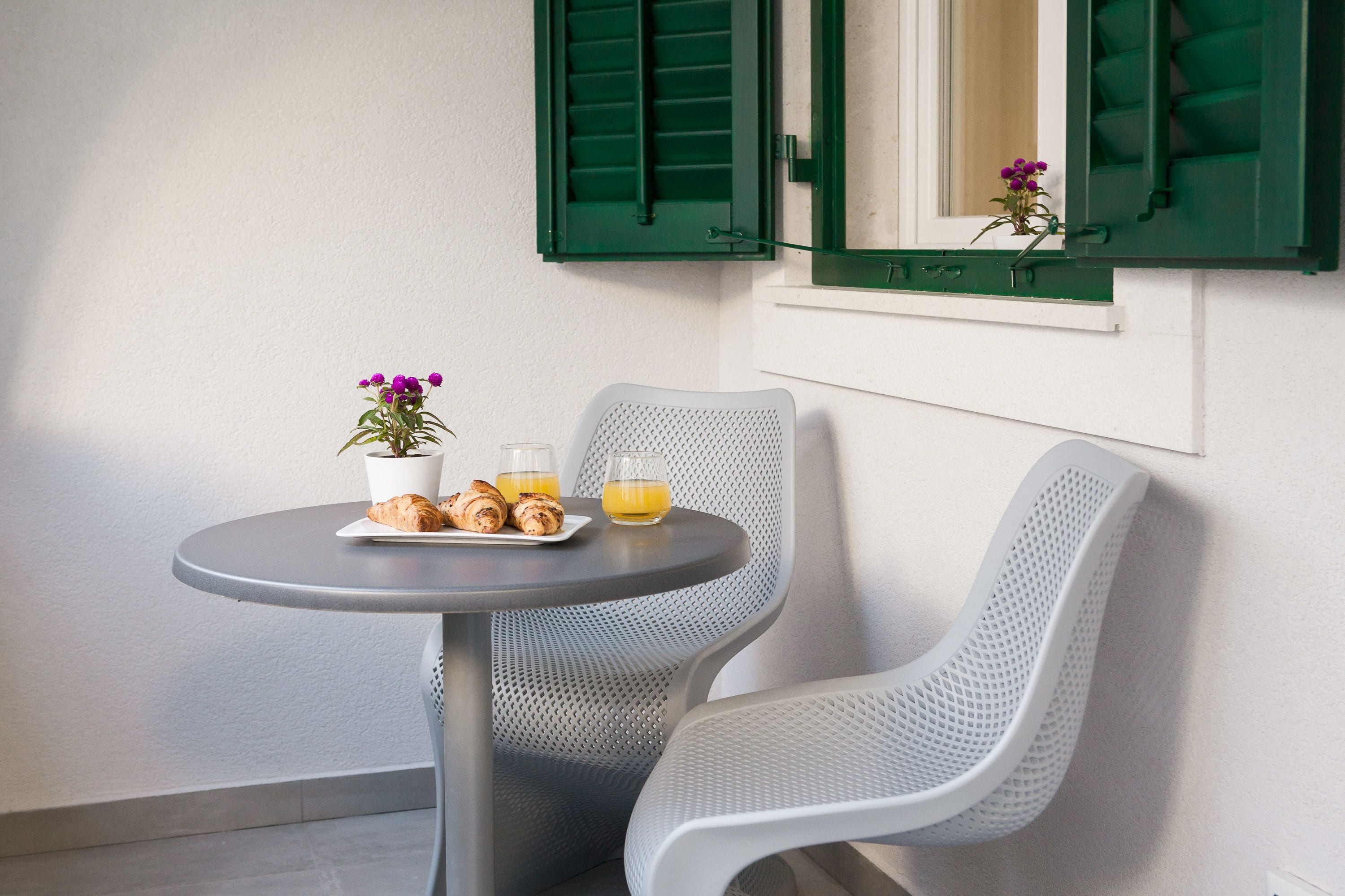 A small round table with a potted plant, croissants, and two glasses of orange juice.