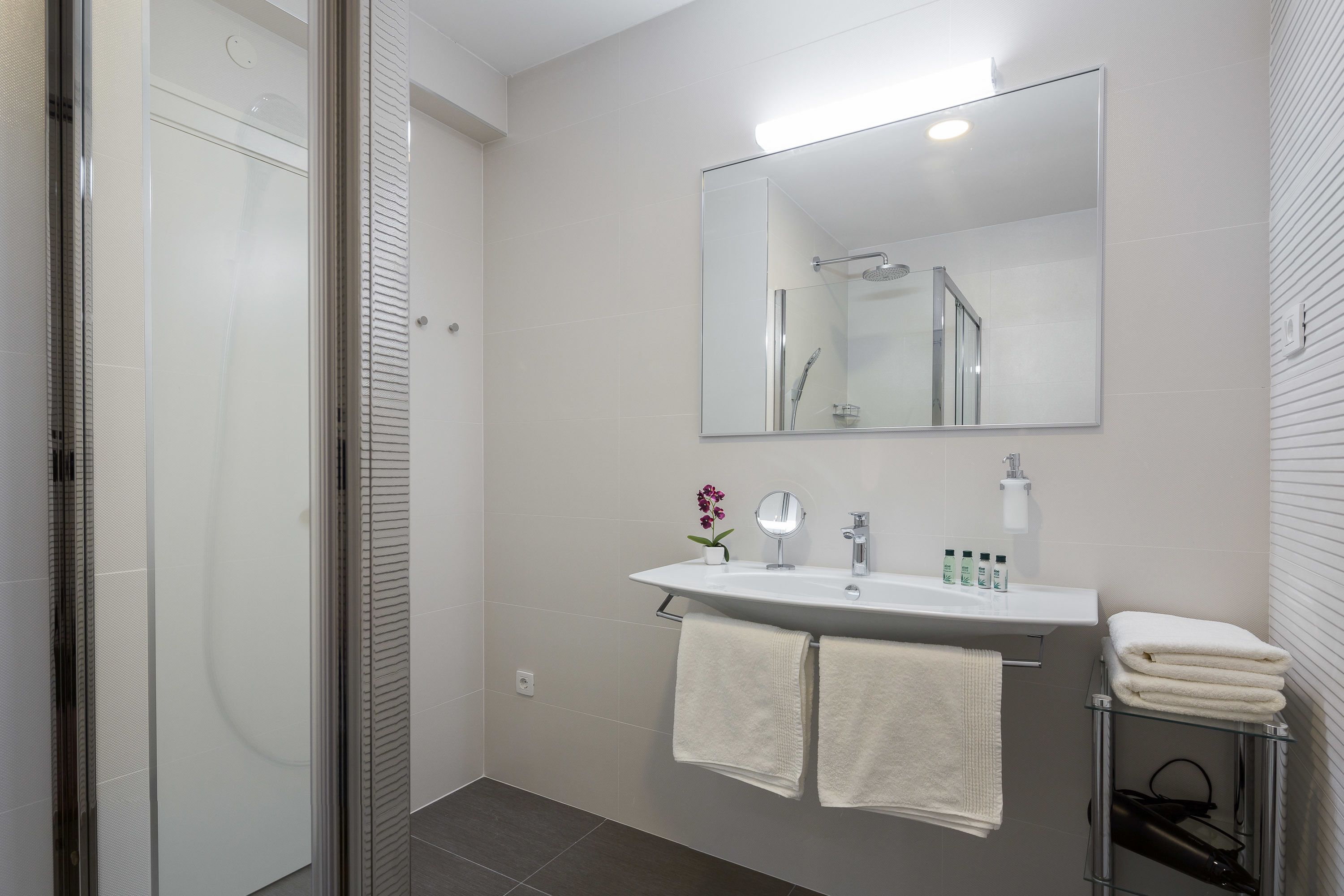 A modern bathroom with a glass shower enclosure, a white sink with a mirror above it, and two towels hanging on a rack.