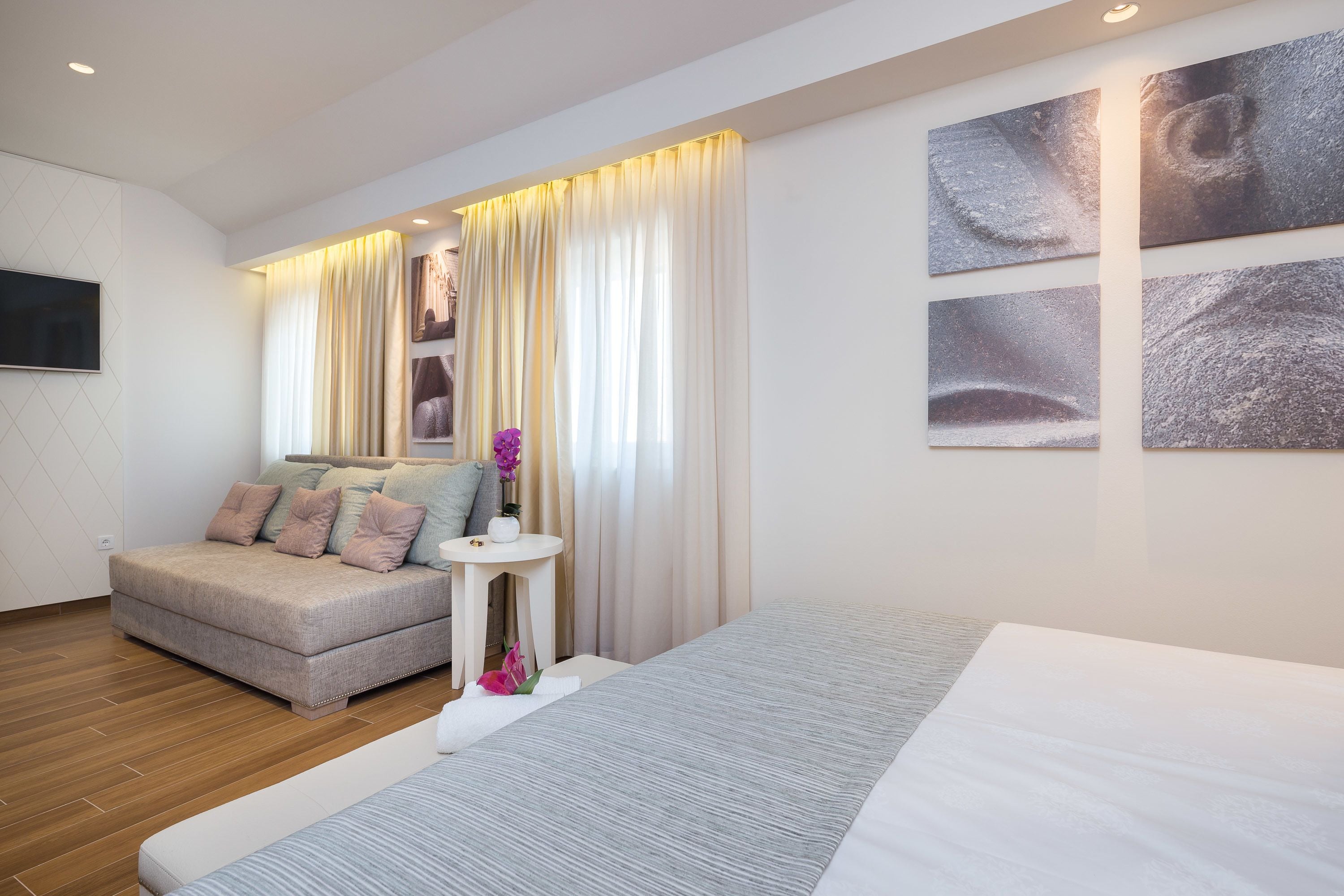 Una habitación de hotel moderna con sofá, cama, una mesita con un florero y obras de arte en la pared.