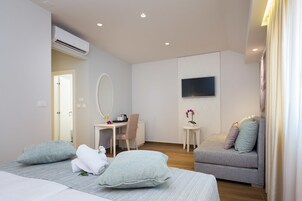 Una habitación de hotel moderna con una cama, un sofá, un escritorio con una silla, una mesita con una planta y un televisor montado.