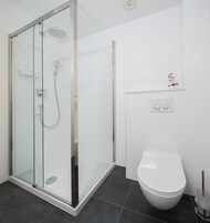 Ein modernes Badezimmer mit einer gläsernen Duschkabine, einer weißen Toilette und einem kleinen Topfpflanzen an der Wand.