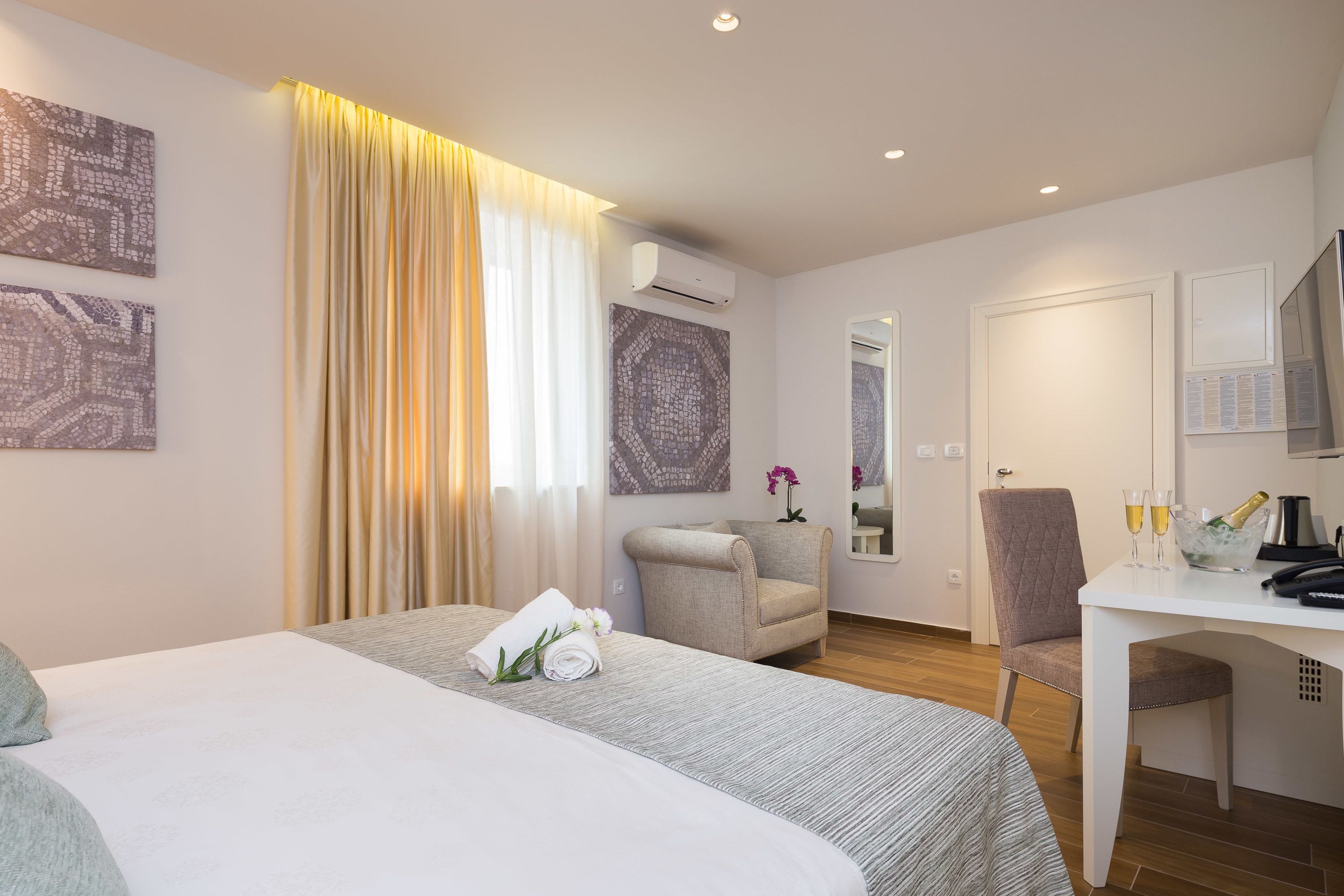 A hotel room with a bed, a desk with a chair, a minibar, and a mirror.