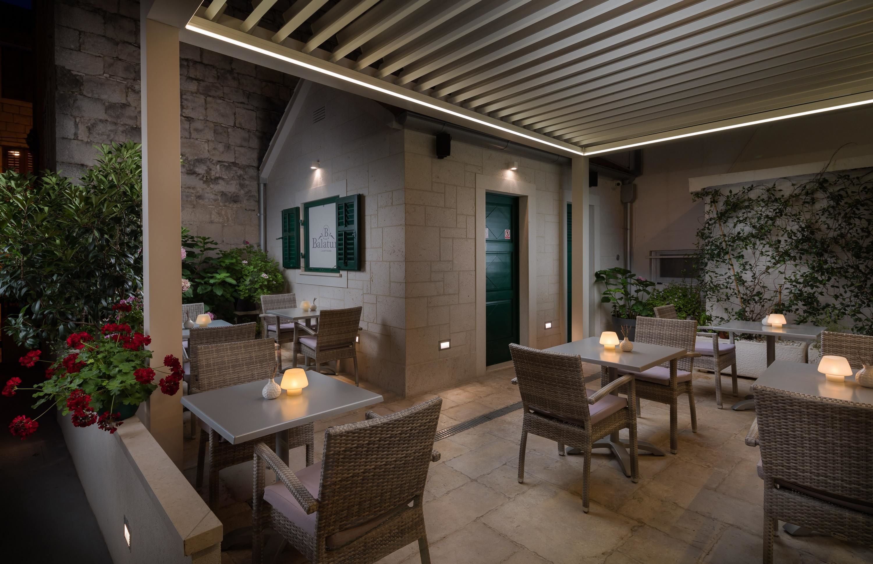 An outdoor dining area with wicker tables and chairs, a stone wall, and green shutters.