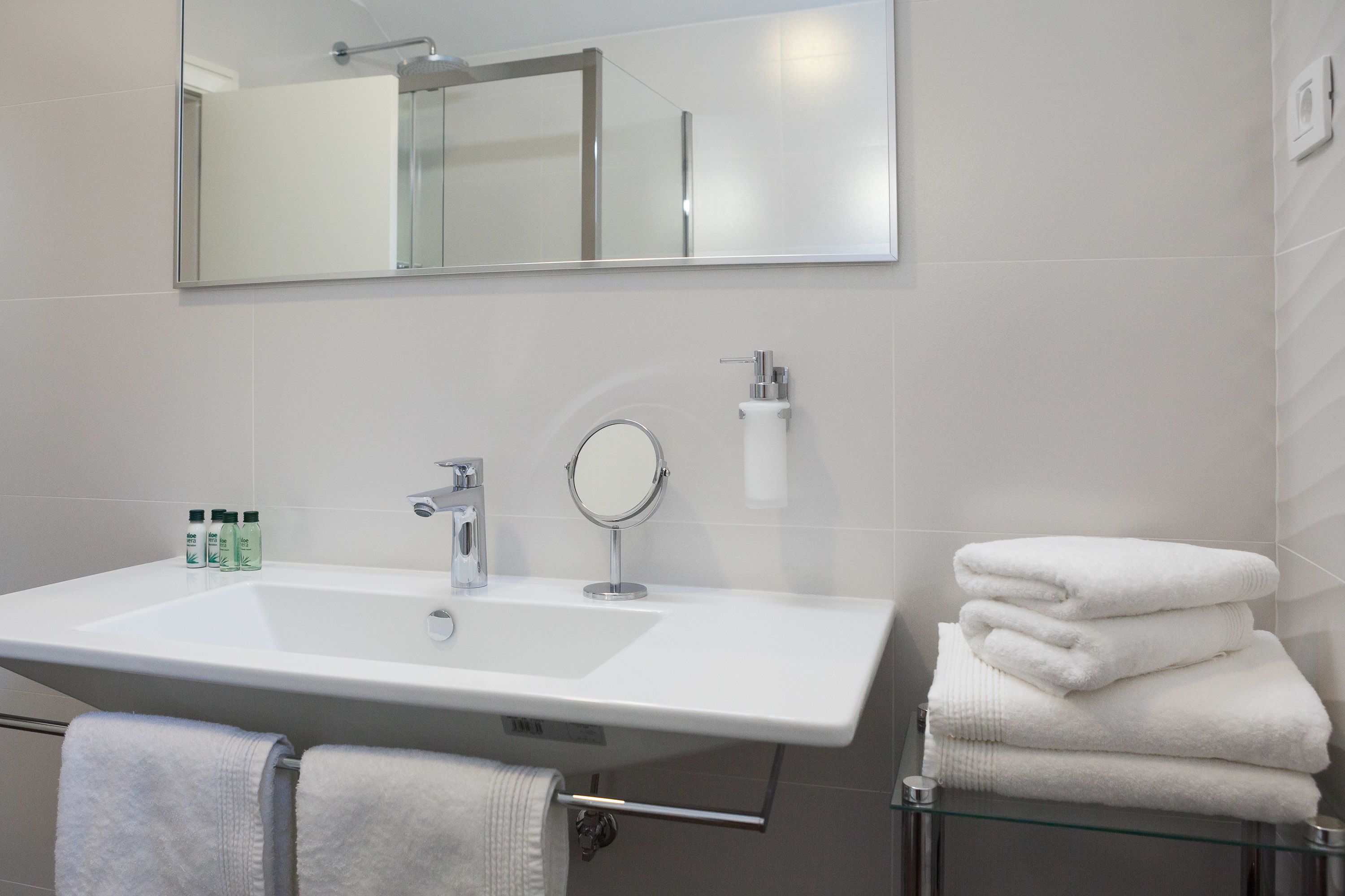 A bathroom with a large white sink, a mirror, and a glass shelf holding folded towels.
