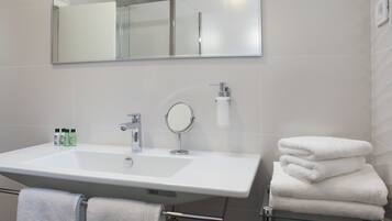 A bathroom with a large white sink, a mirror, and a glass shelf holding folded towels.