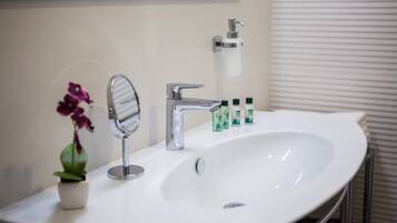 A bathroom with a white sink, a mirror, a faucet, and a small potted orchid.