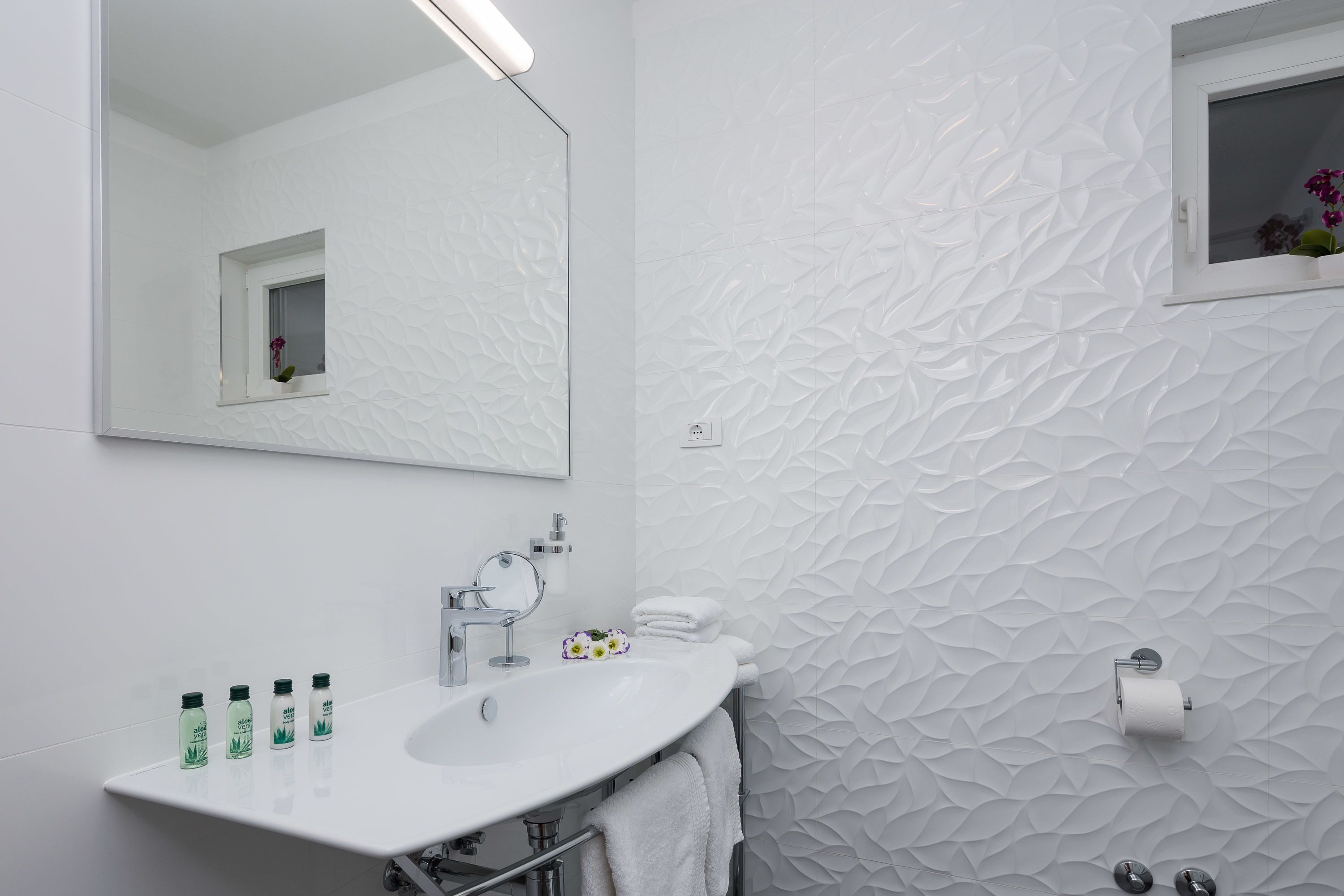 A modern bathroom with a white sink, mirror, and textured wall.
