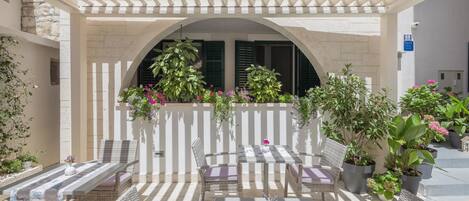 An outdoor patio with wicker furniture, potted plants, and a pergola structure.