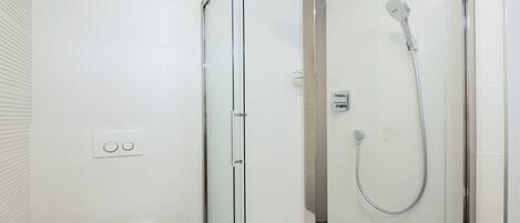 A modern bathroom with a glass-enclosed shower, a white toilet, and a small stool.