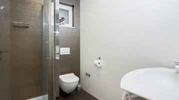 A modern bathroom with a glass shower enclosure, a toilet, and a sink with a towel hanging on the wall.