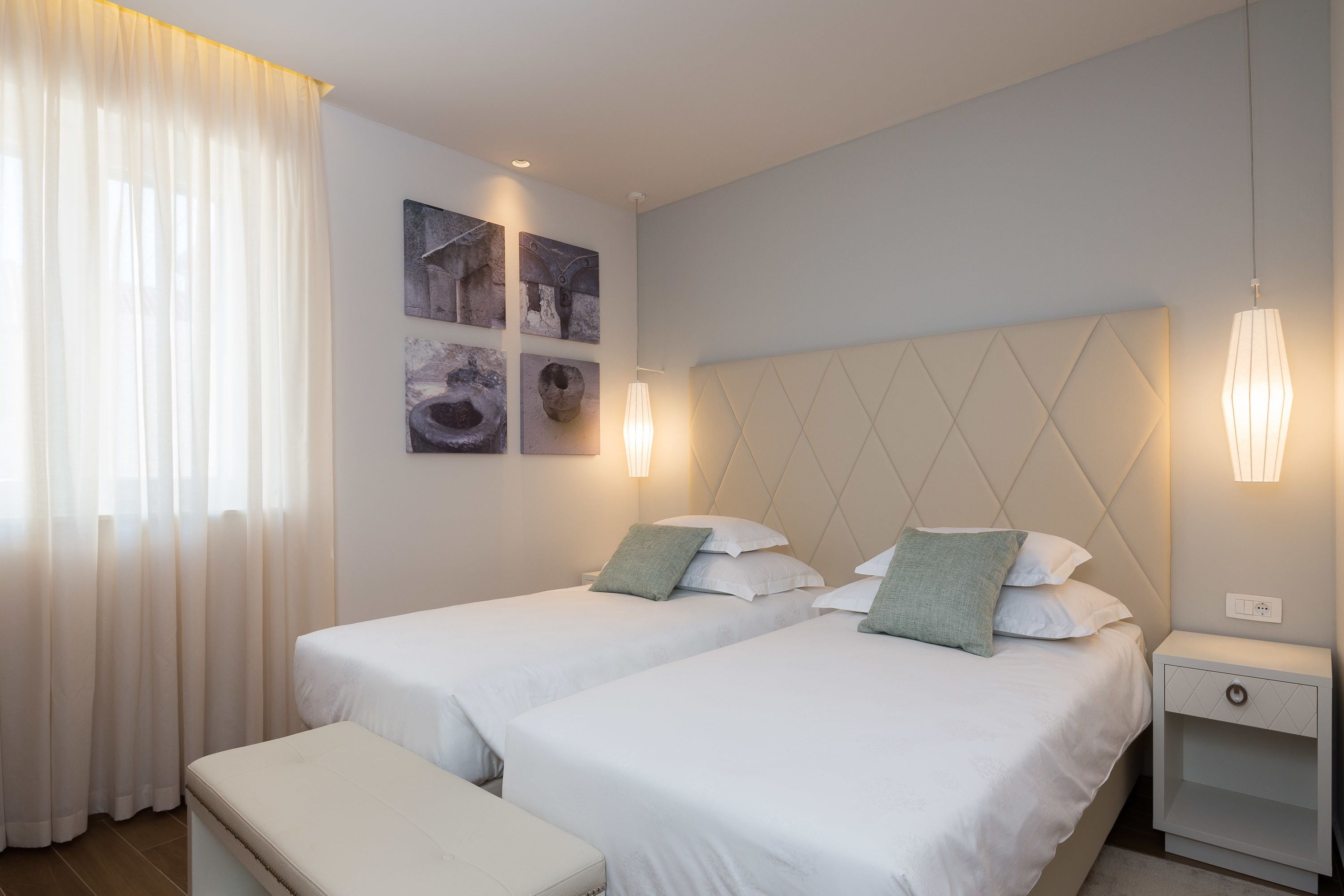 A hotel room with two beds, a bench, and artwork on the wall.