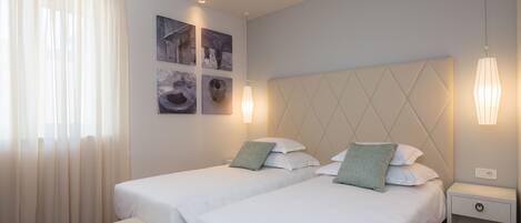 A hotel room with two beds, a bench, and artwork on the wall.