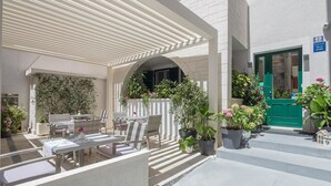 A covered outdoor seating area with wicker furniture, potted plants, and a green door.