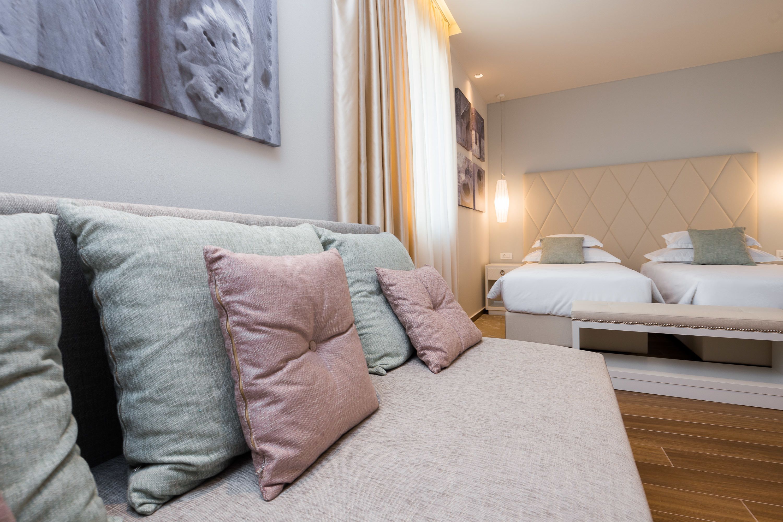 A modern hotel room with a sofa, two beds, and a bench.